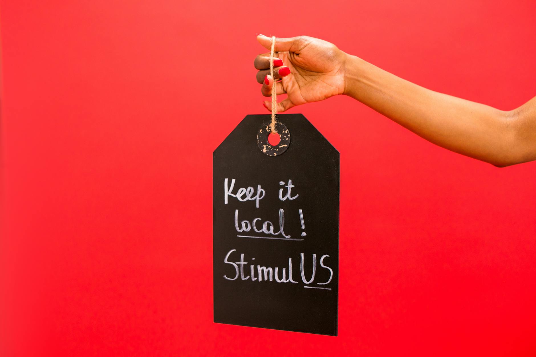 Dłoń trzymająca tabliczkę Keep it local! StimulUS na czerwonym tle