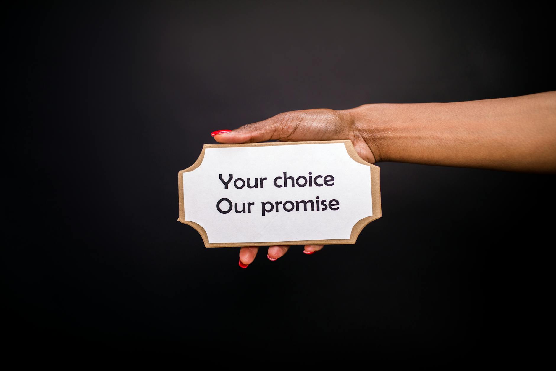 Dłoń trzymająca tabliczkę Your choice, Our promise na ciemnym tle