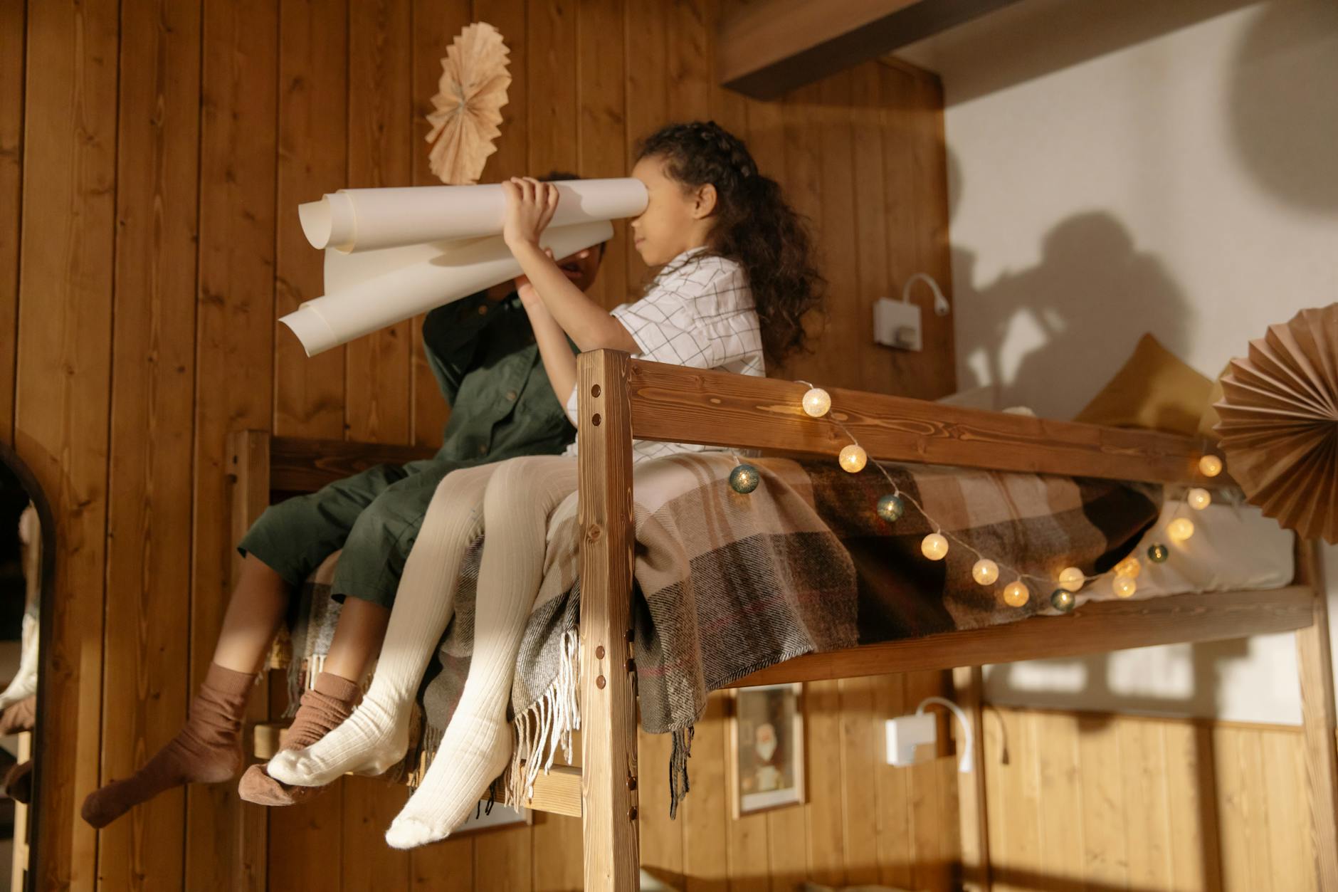 Dwoje dzieci bawi się na udekorowanym drewnianym łóżku piętrowym