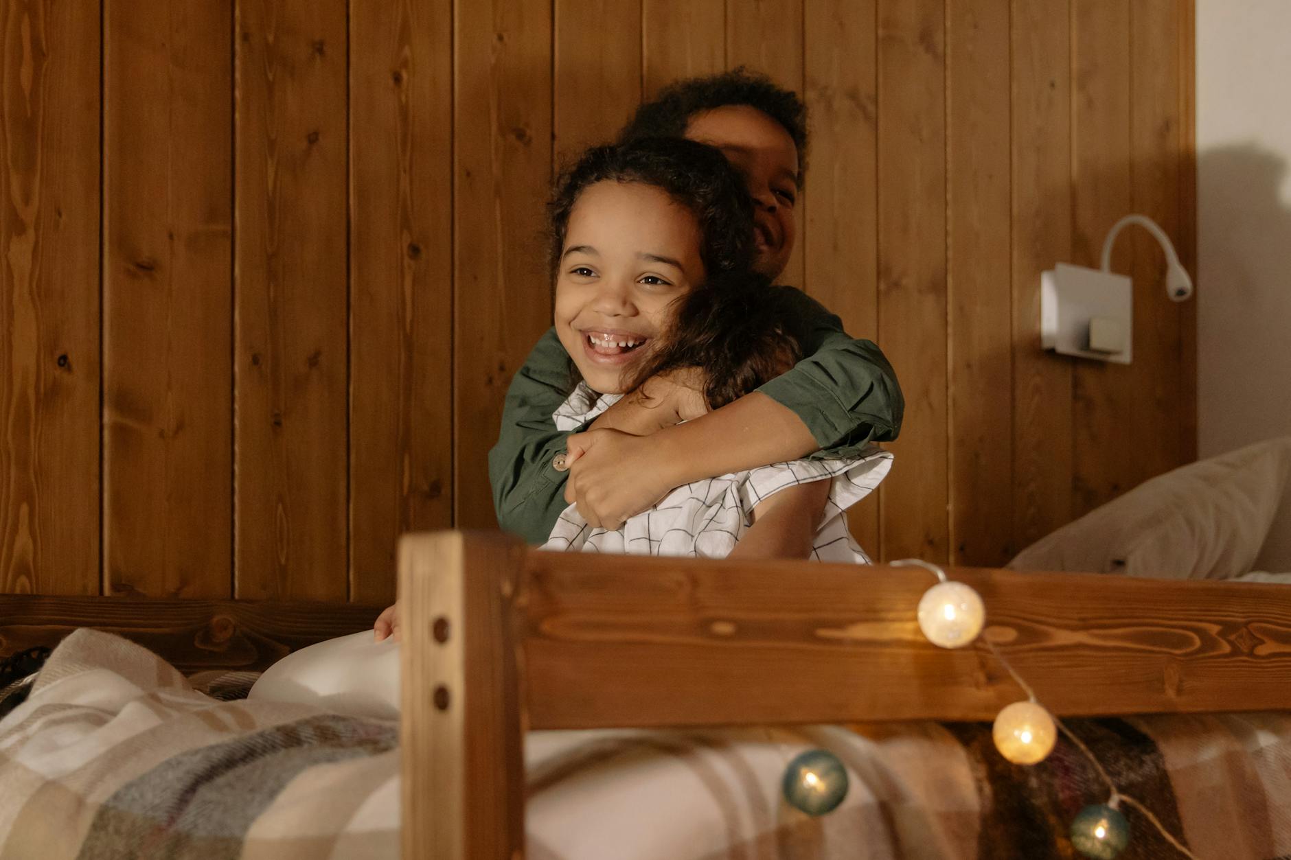 Dwoje roześmianych dzieci przytula się na przytulnym łóżku w ciepłym świetle