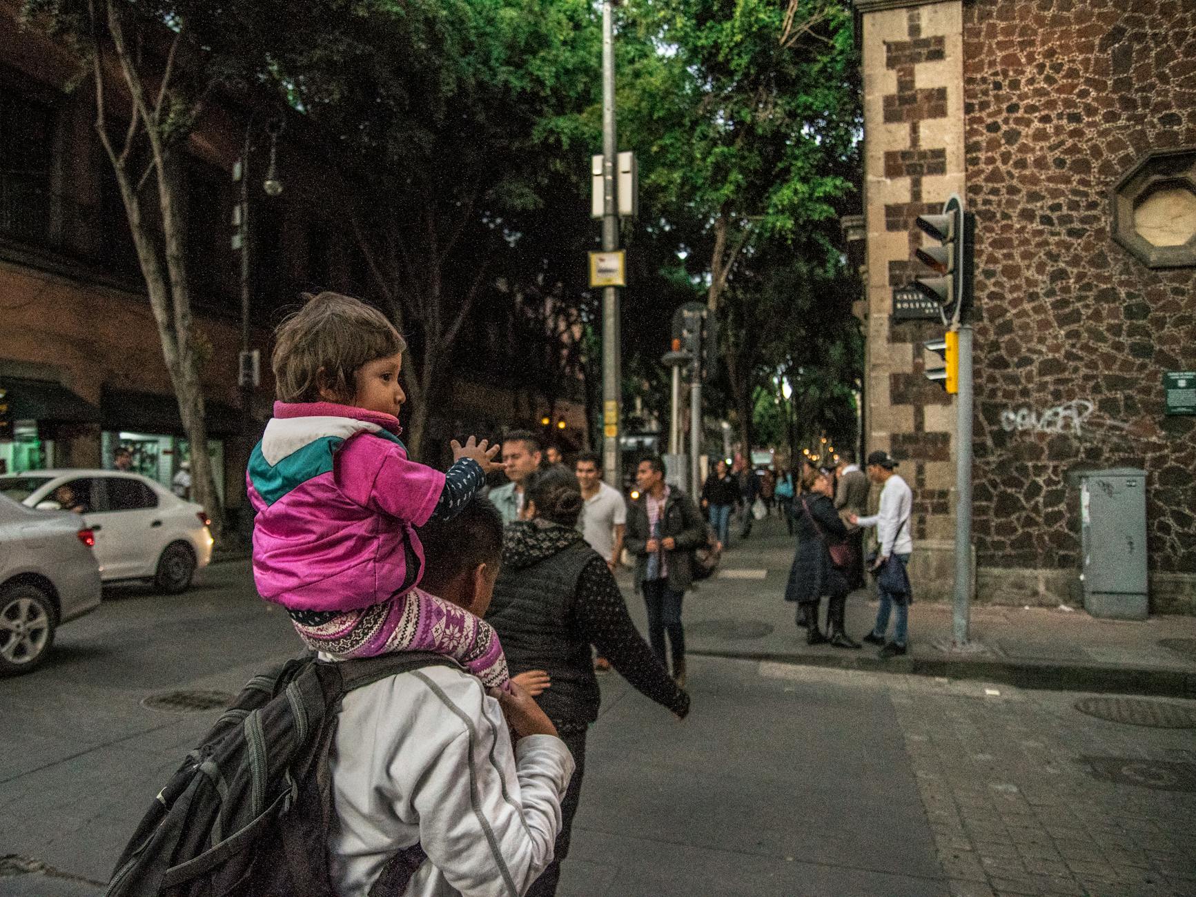 Tata niosący dziecko na gwarniej ulicy w Meksyku