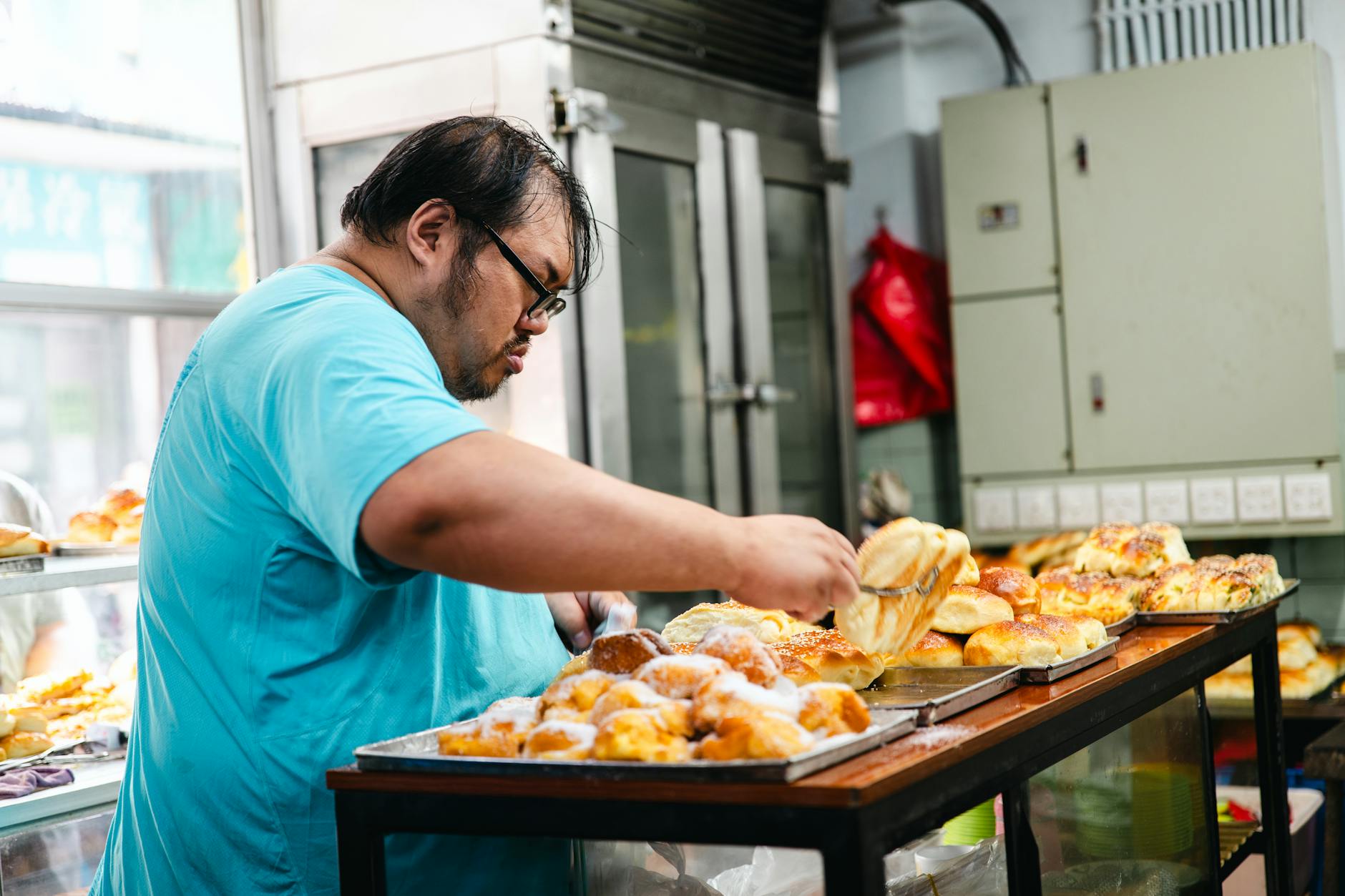 Piekarz w niebieskiej koszuli układa świeże pieczywo w tradycyjnej piekarni