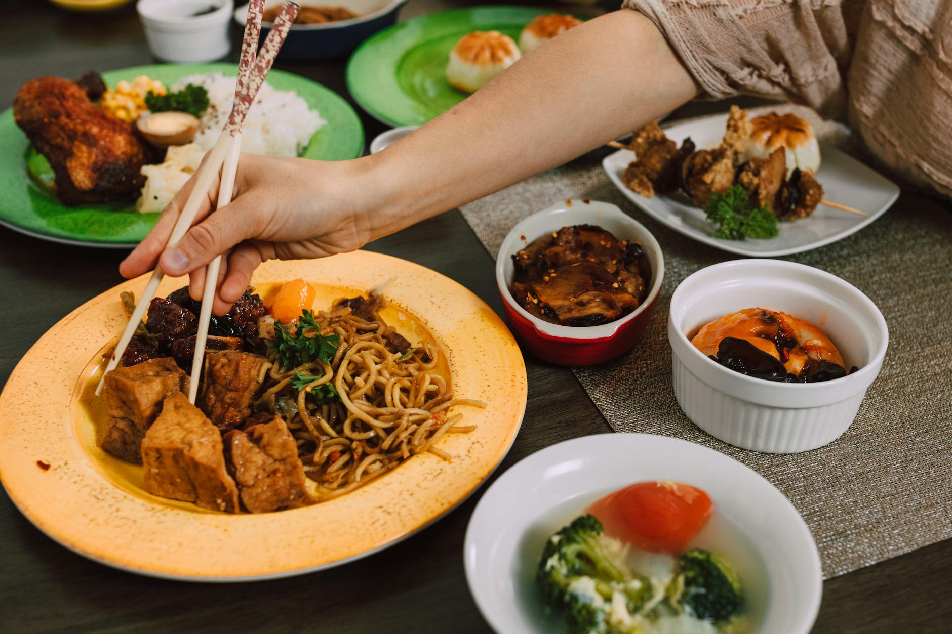 Ręka pałeczkami sięga po kolorowe wegetariańskie dania kuchni azjatyckiej