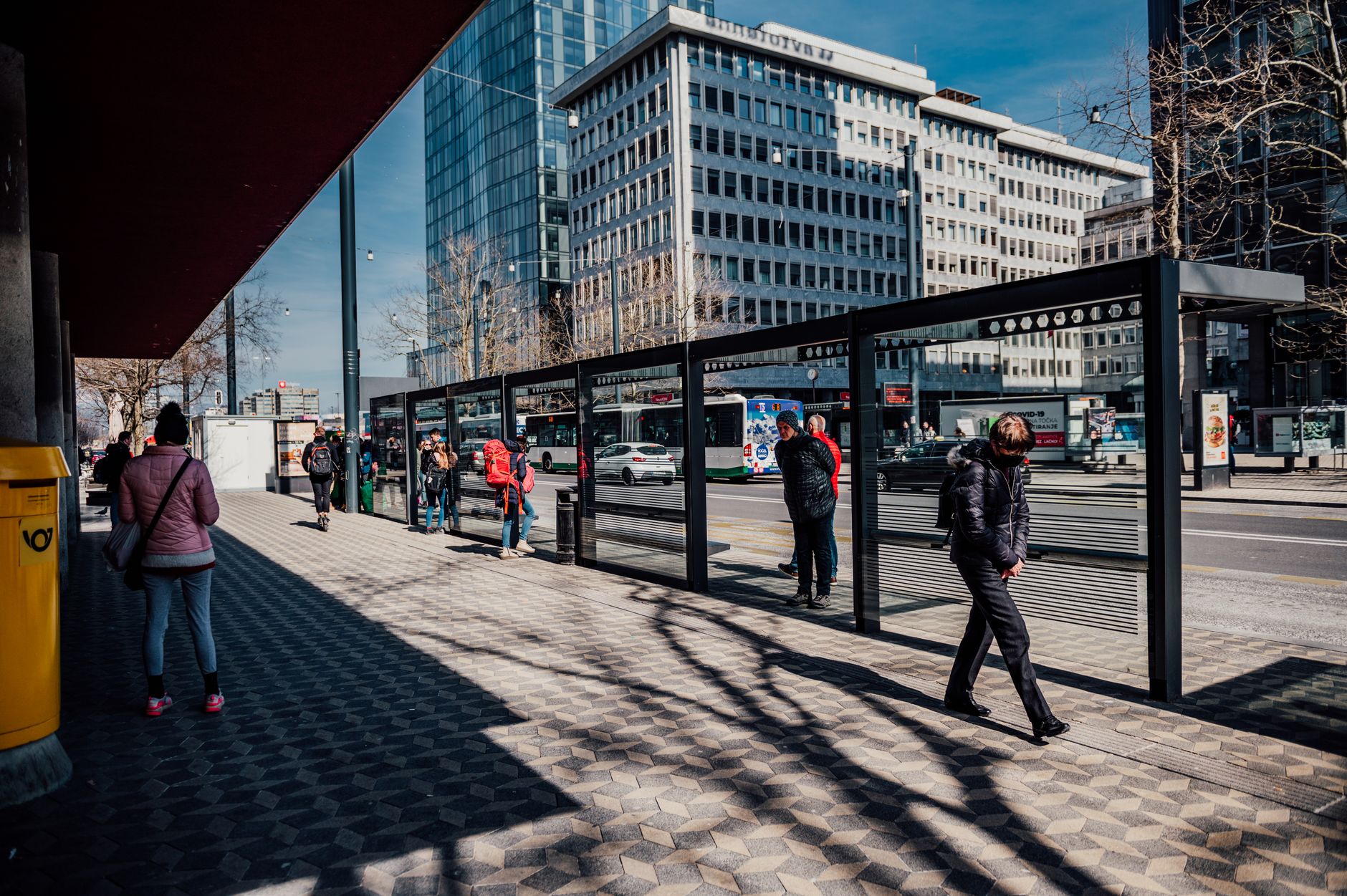 Pasażerowie czekają na przystanku autobusowym wśród nowoczesnych biurowców