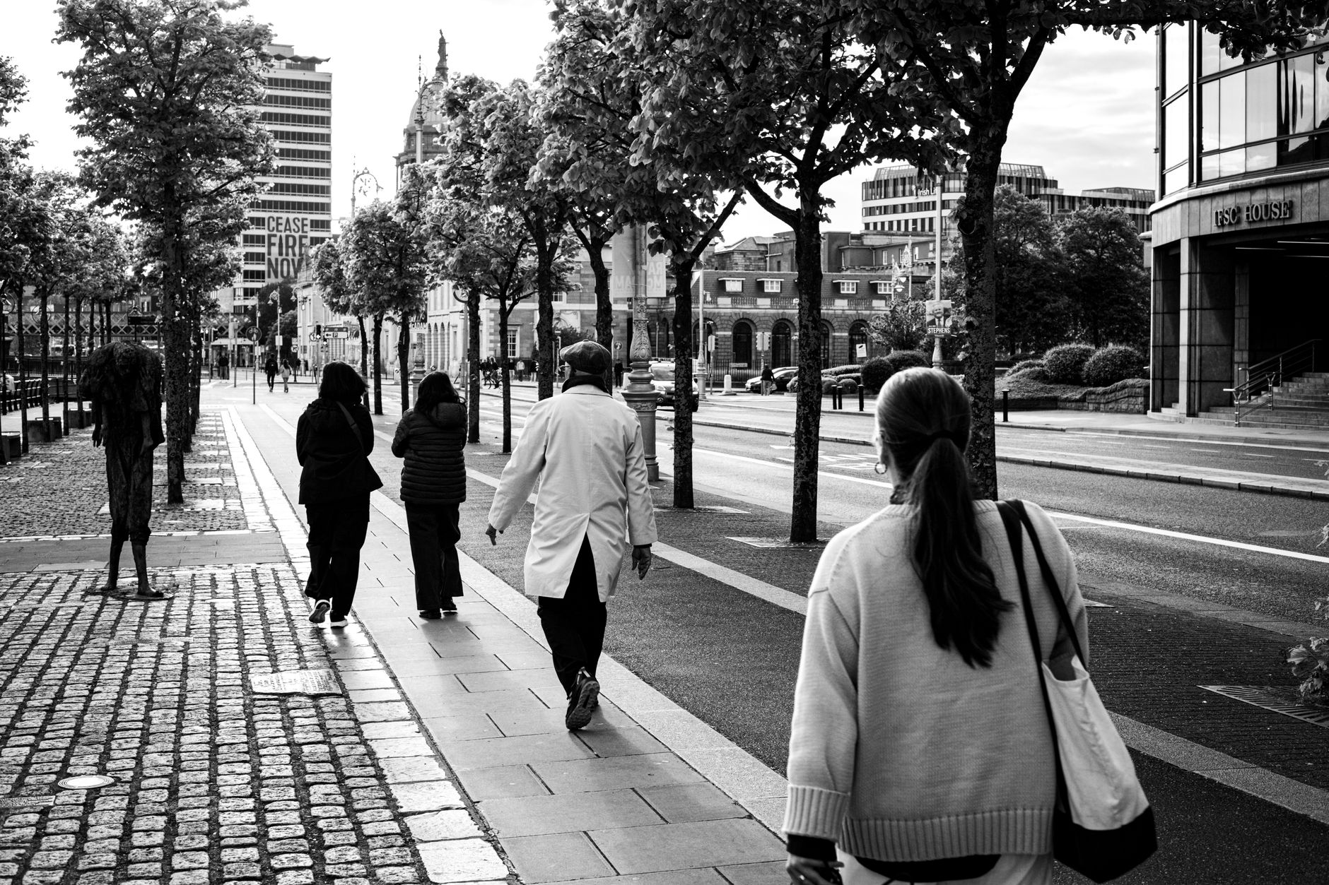 Przechodnie na ulicy w Dublinie obok rzeźb upamiętniających głód